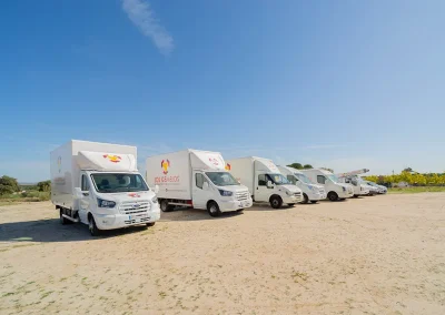 Camiones de Mudanzas y Guardamuebles Los Gemelos estacionados en fila en un campo.