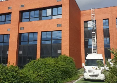 Furgoneta de mudanzas Los Gemelos estacionada frente a un edificio universitario con una larga escalera desplegada.