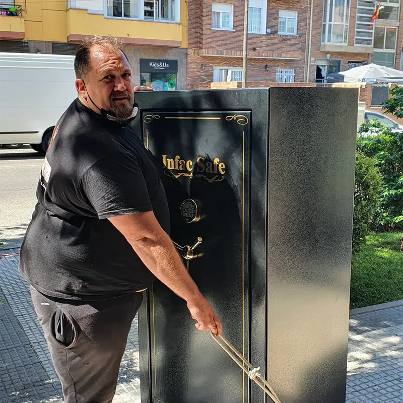 Los Gemelos Mudanzas transportando una caja fuerte negra grande en la calle, con edificios de fondo.