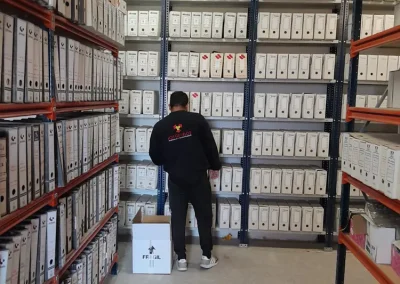 Un trabajador de mudanzas de Los Gemelos embalando cajas en un almacén con estanterías llenas de archivos
